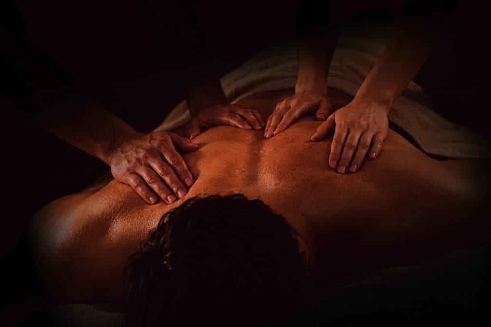 Nahaufnahme einer Vierhand-Rückenmassage im warmen, gedämpften Licht